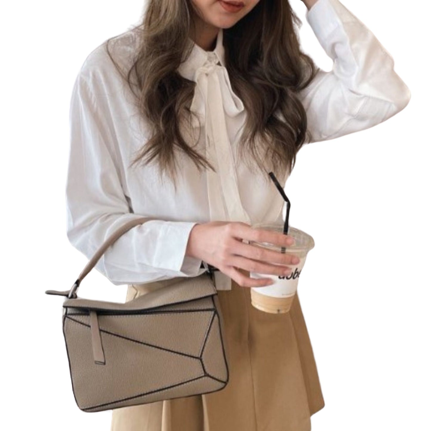 Woman carrying Amy vegan leather handbag in Sand by top handle, resting in the crook of her arm; features geometric panels.