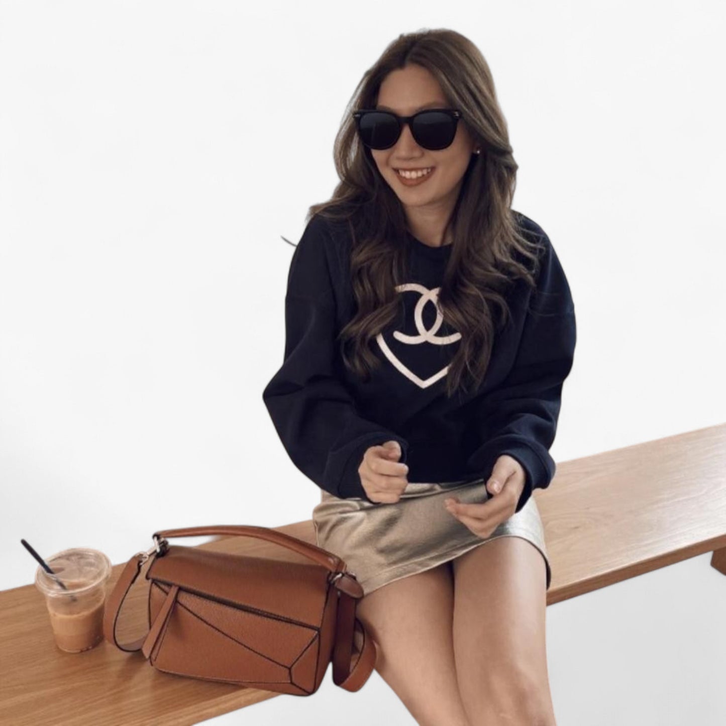A woman sits beside a brown geometric-shaped handbag with a top handle and a strap.