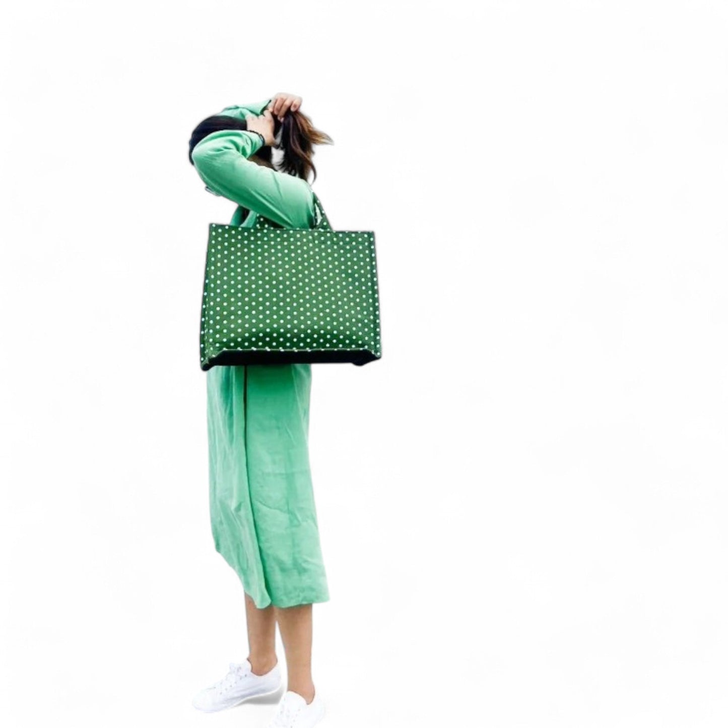 A model wearing a green tote bag with small white polka dots on their shoulder.
