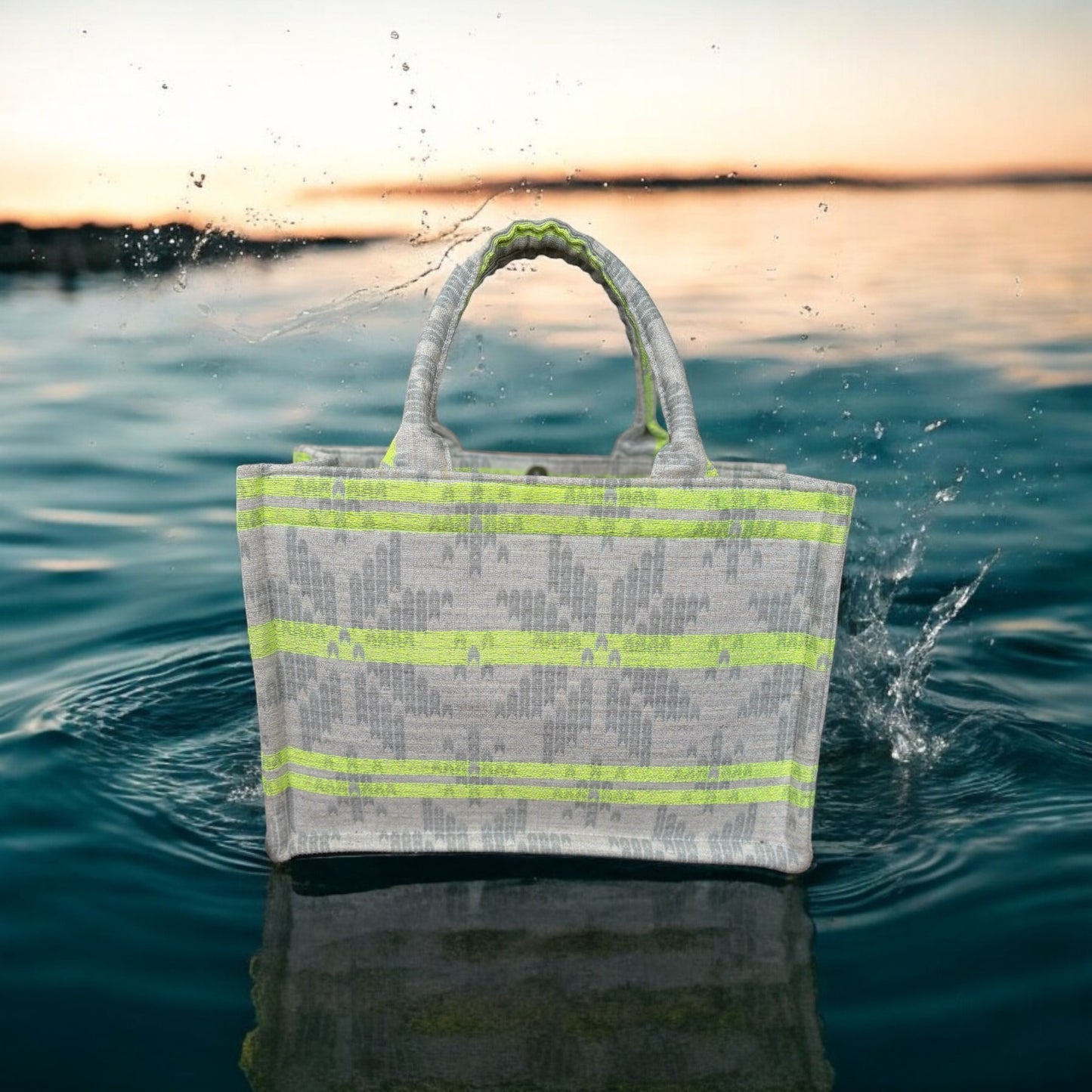A tote bag with neon green stripes on light grey jacquard fabric, sitting on top of a pool of dark blue water.