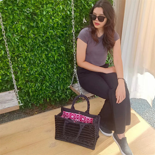 Woman sitting on a swing with a spacious black everyday tote bag on the floor in front of her.