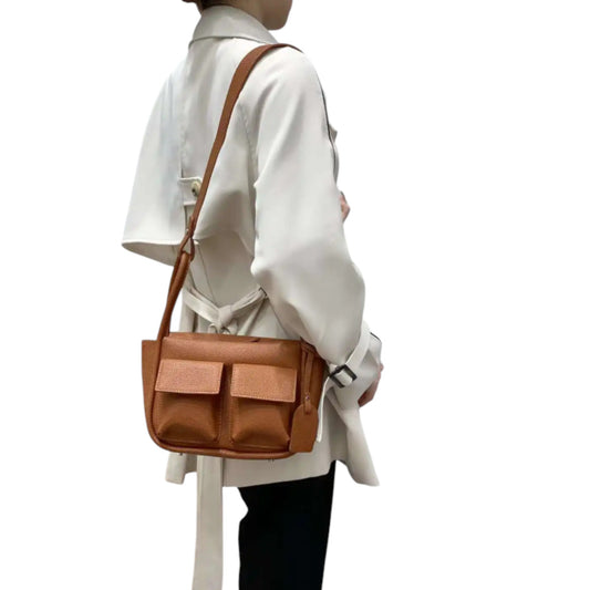 Woman wearing a brown faux leather Dougie shoulder bag with a long strap, worn over shoulder, features two front flap pockets.