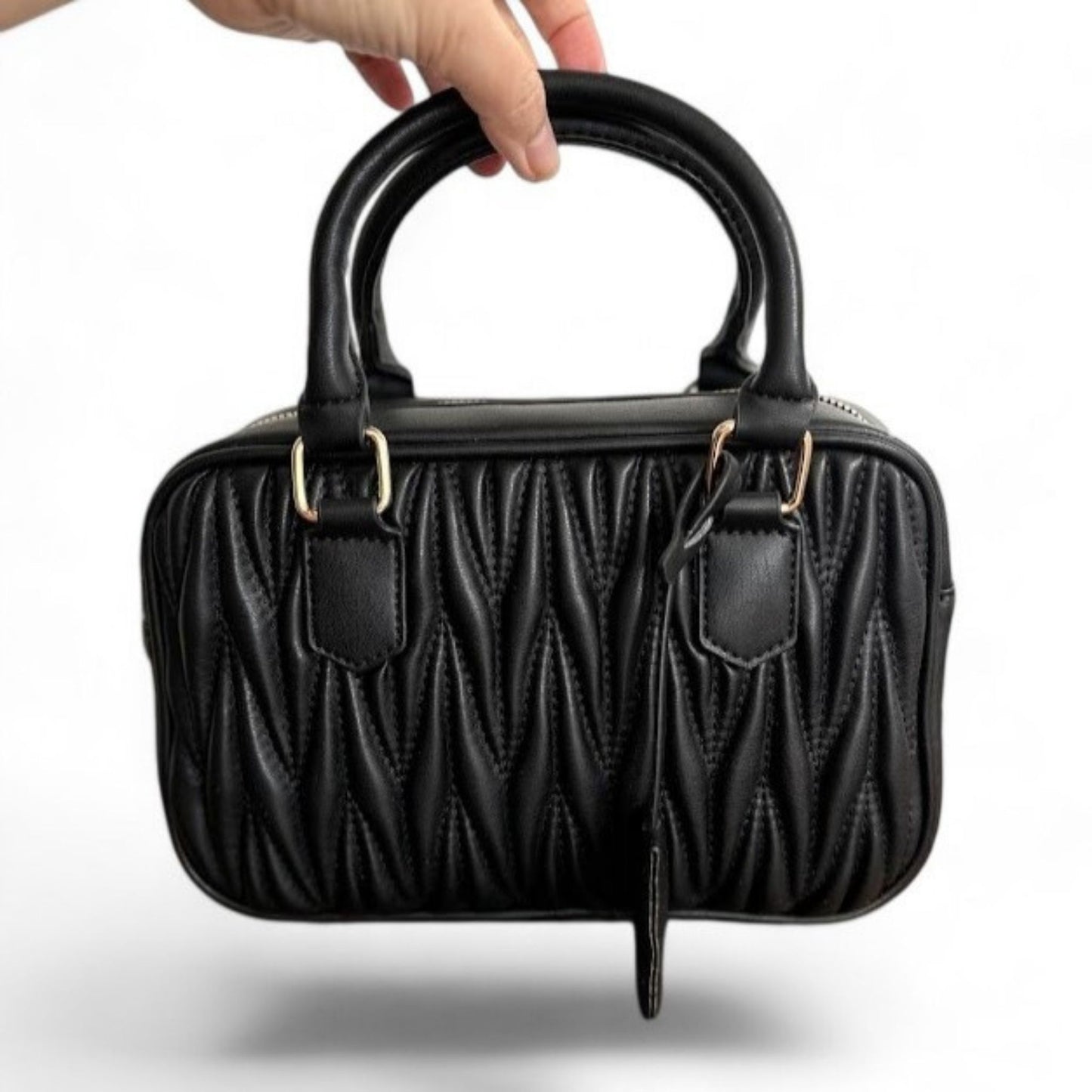 A hand carrying a black handbag with a quilted pattern, featuring gold-tone hardware & top handles.