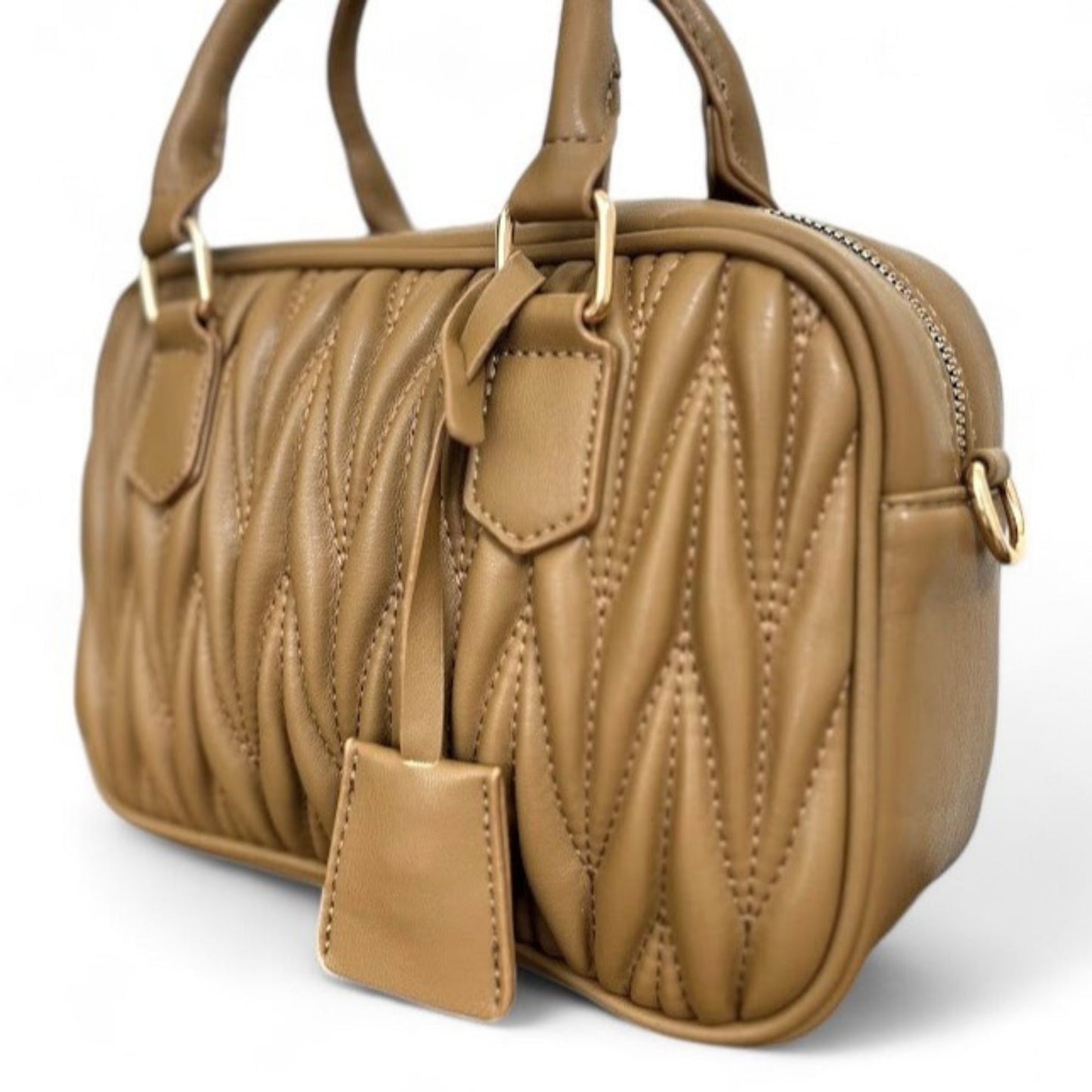 Close-up of a caramel handbag with a quilted pattern, gold hardware, top handles, and a bag tag.