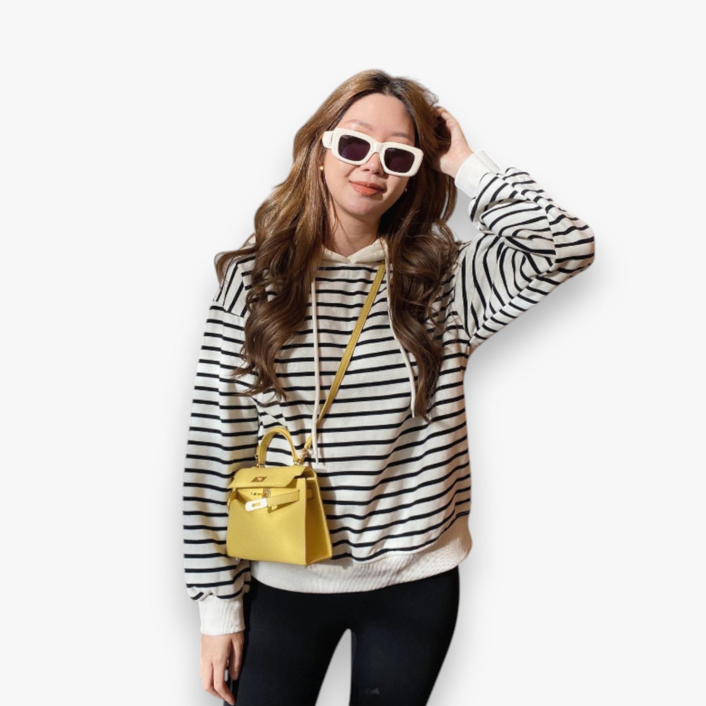 Full-body image of a young woman posing in a fashionable street style look, carrying a yellow crossbody mini bag.