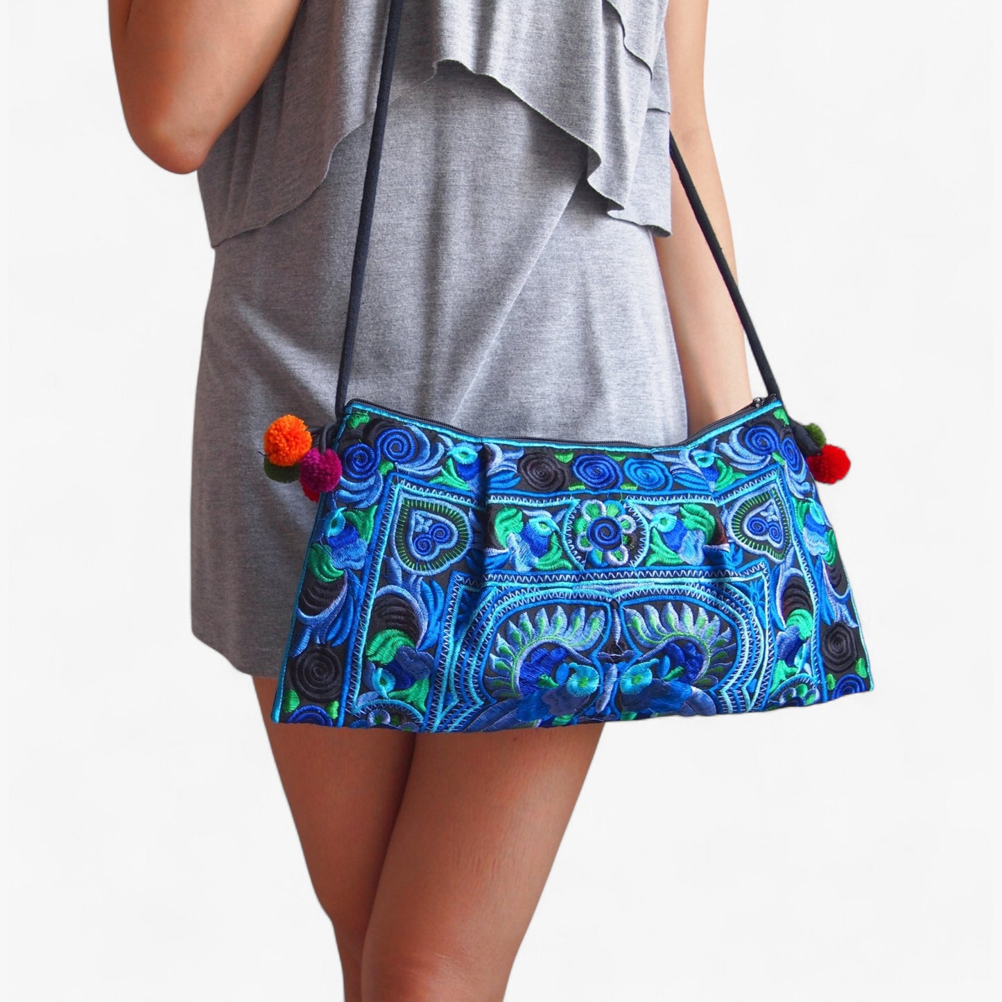 Teal peacock and floral-patterned crossbody bag with colourful pom-poms and a cord strap.