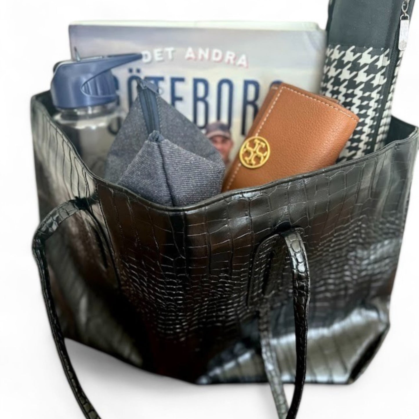 Open black tote bag showing contents including a book, wallet, and water bottle.