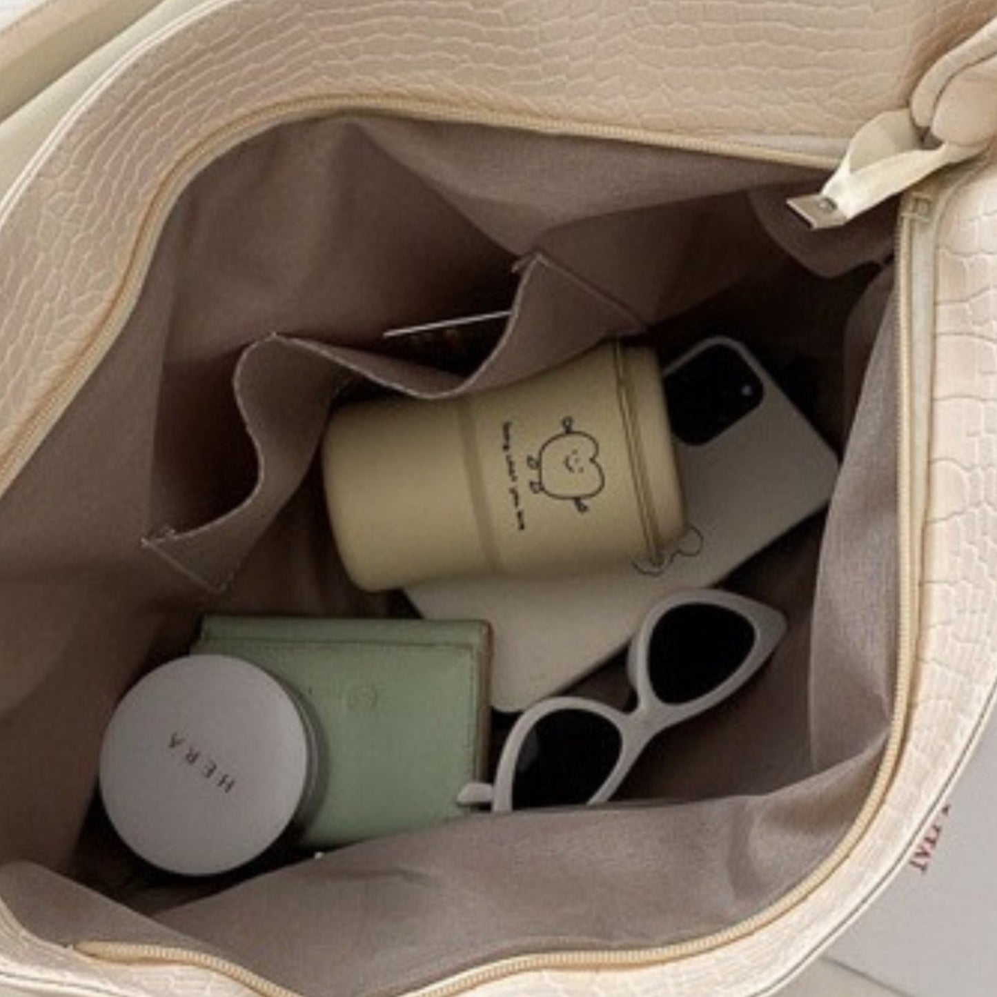 Opened off-white croc tote with sunglasses, phone, and wallet inside, showing internal slip pocket.