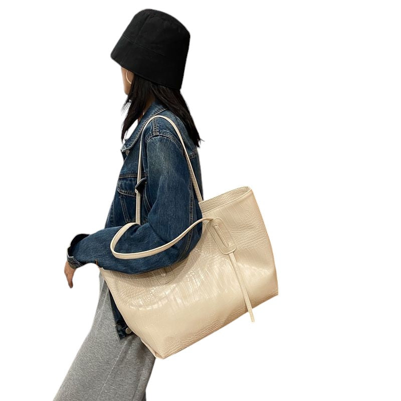 A woman is carrying an off-white croc-embossed vegan leather tote bag over her shoulder.