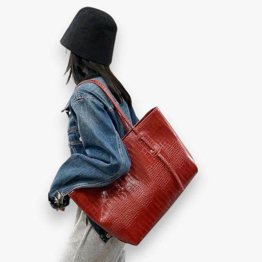 A model carrying a spacious and versatile, burgundy, crocodile-embossed vegan leather tote on her shoulder.