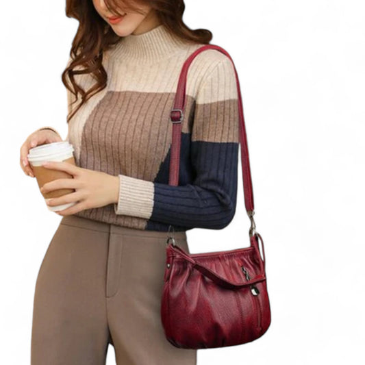 A woman is carrying a maroon bag with a long strap over her shoulder and a folded handle at the front.