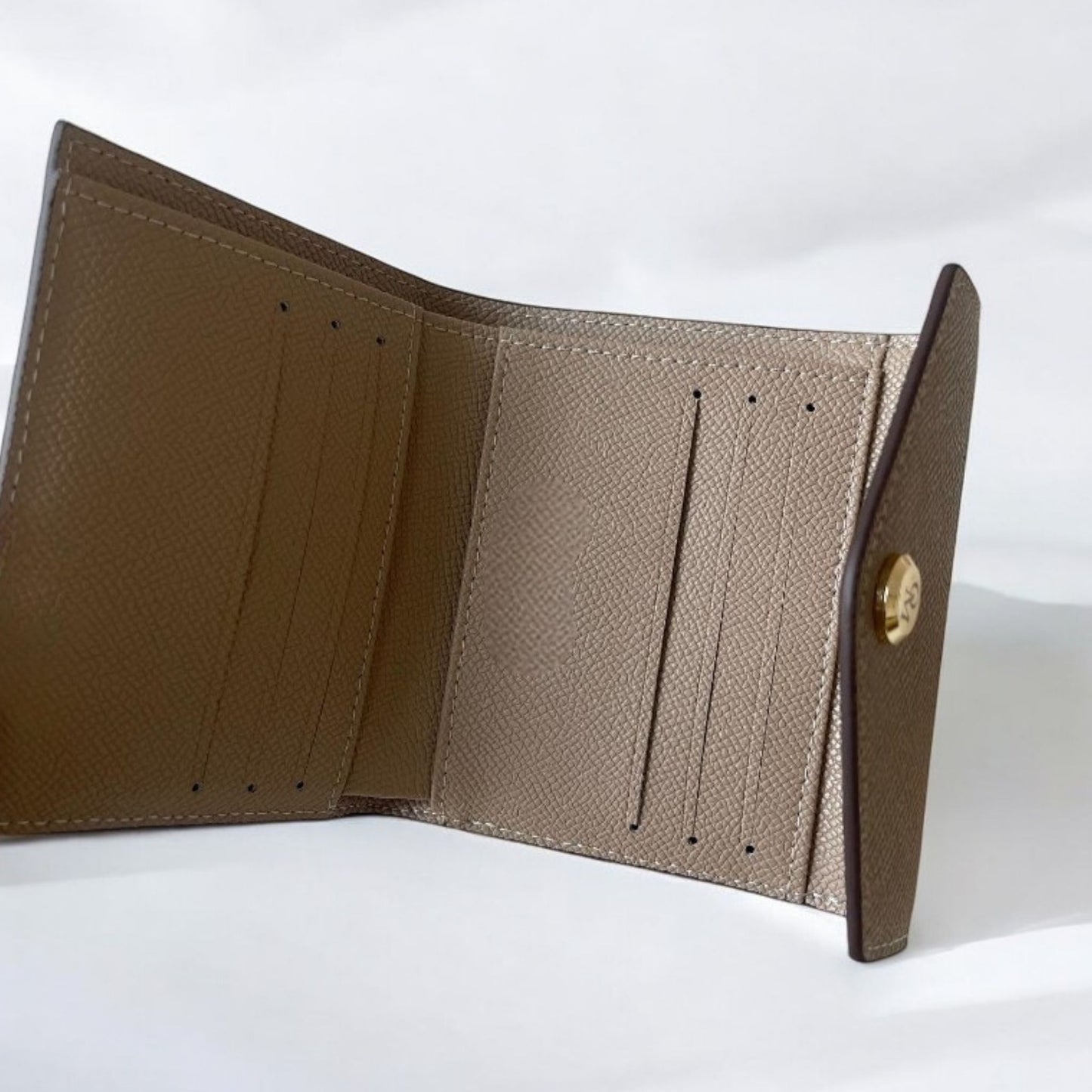 Interior of a tri-fold khaki wallet displaying card slots, envelop-style flap, and smooth gold button.