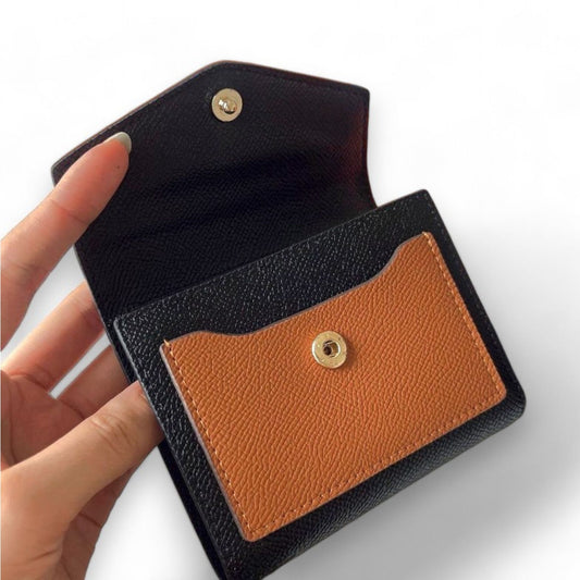 A hand holding a compact small brown/black grain-textured leather wallet with a gold snap button.