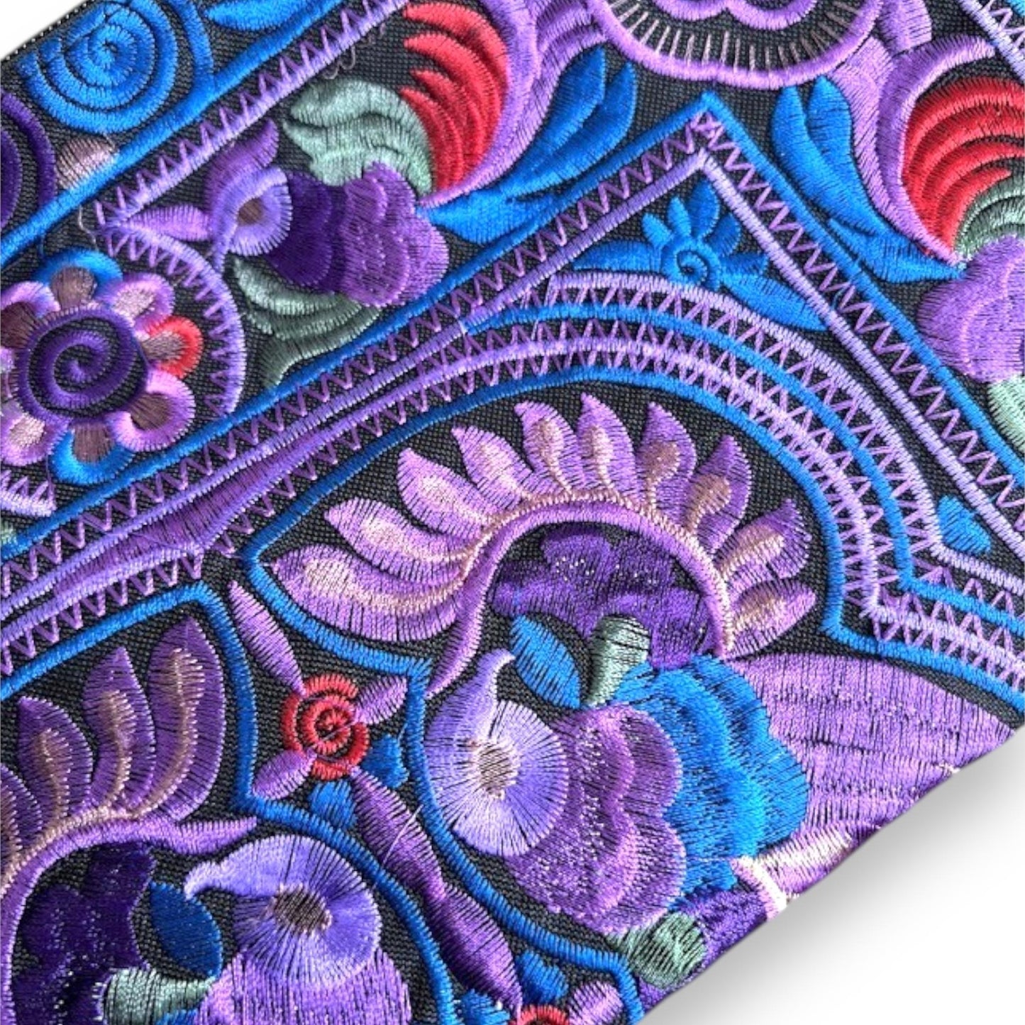 Close-up of intricate embroidered fabric with bird and floral patterns in purple, blue, and red.