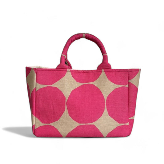 A tote bag with top handles and expanded side panels features rows of large dots in hot pink on beige fabric.