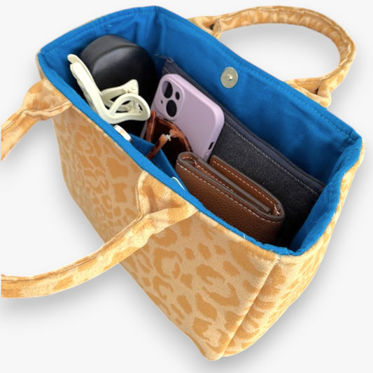 A vibrant yellow leopard-print bag with top handles and a blue interior containing everyday items.