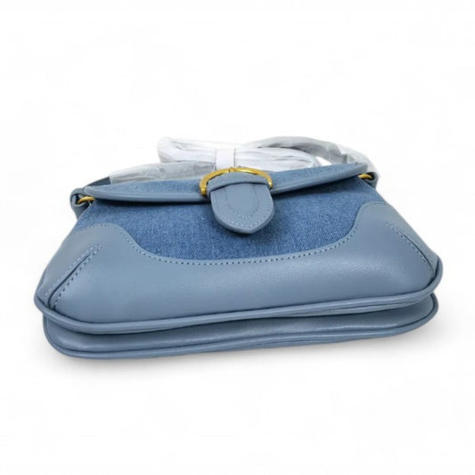 A blue denim bag with leather trim lies flat, showcasing two compartments and a brass-tone buckled flap.