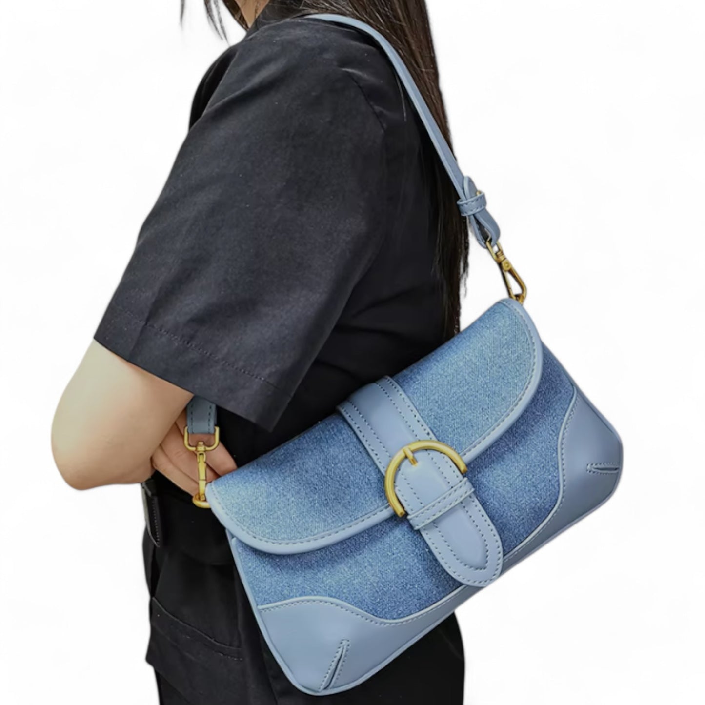 A woman carries a blue denim bag with leather trim and brass-tone details on her shoulder.
