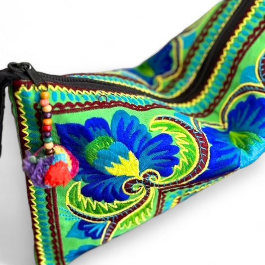 A wristlet bag with a mini pompom top zipper, and peacock and floral patterns in vibrant green and blue.