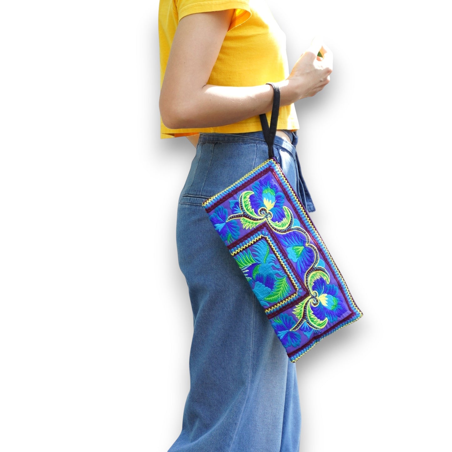 Model holding a green peacock oversized wristlet with vibrant Hmong embroidery and bold patterns.