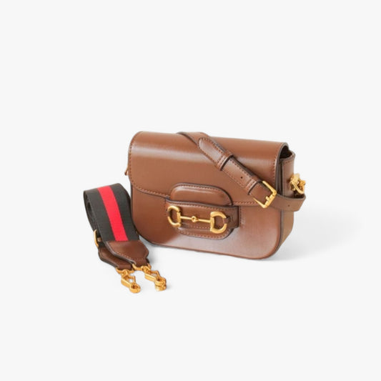 Brown leather bag with gold accents, featuring a slim, smooth leather strap and a wider nylon strap.