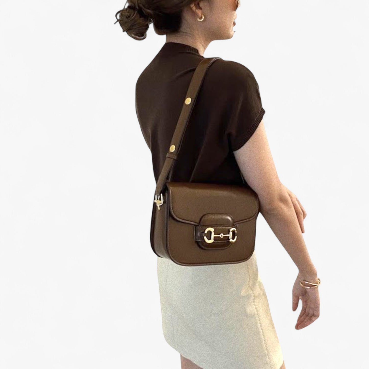 A woman is carrying a brown leather bag with gold accents on her shoulder.