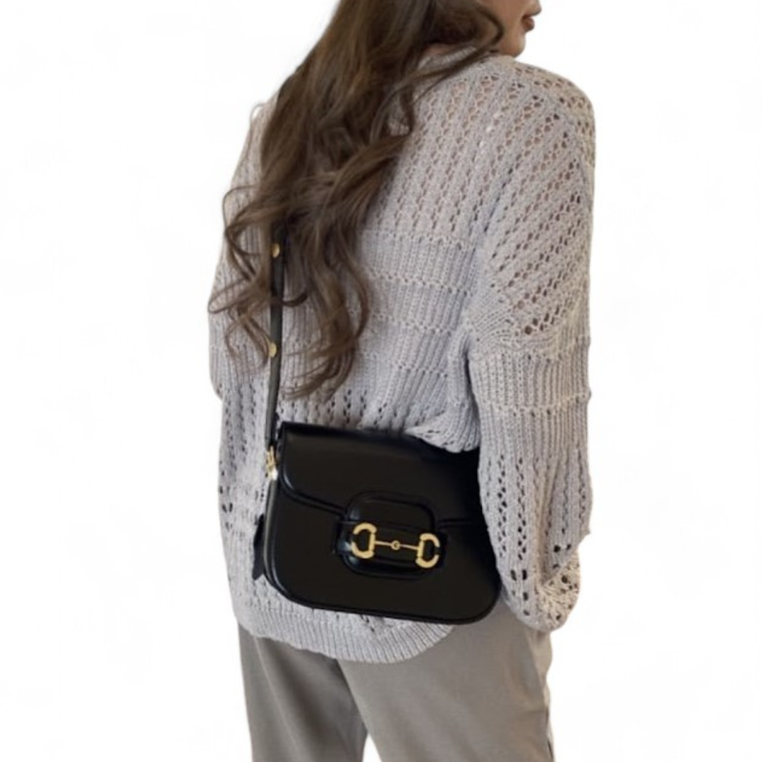A woman wears a black leather bag with gold accents across her body.