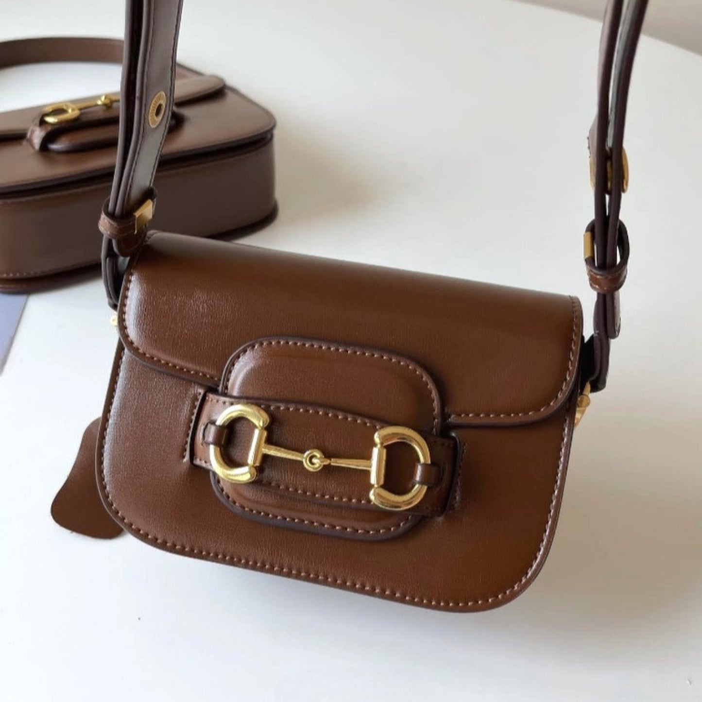 Brown leather handbag with a gold horse bit and a front flap closure.