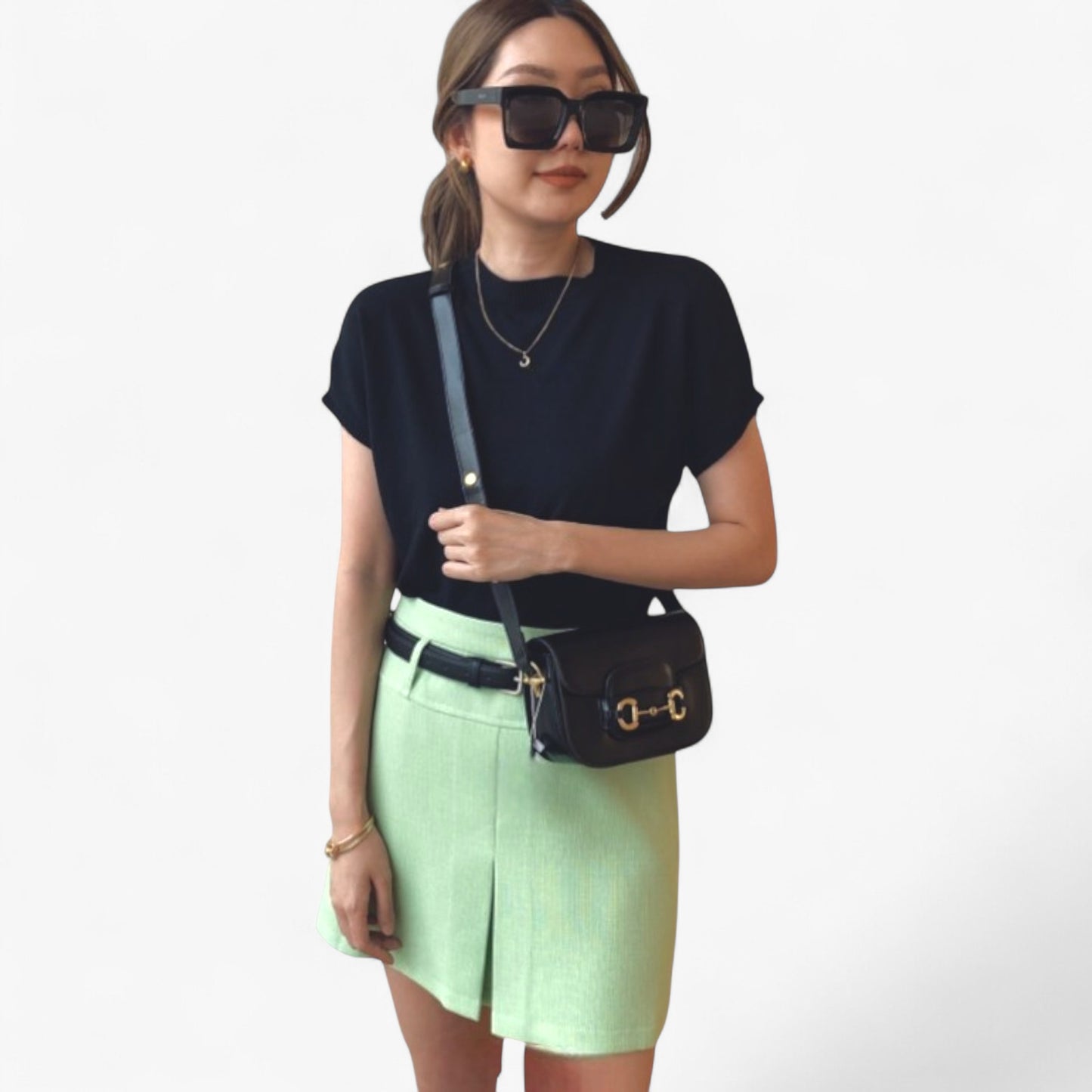 A woman wears a small black handbag with gold accents across her body.