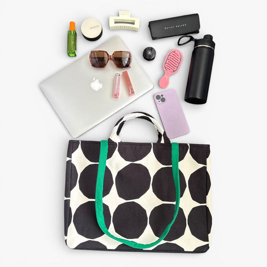 A black and white polka dot tote bag with handles and a green strap. Large enough for a laptop and daily carry.