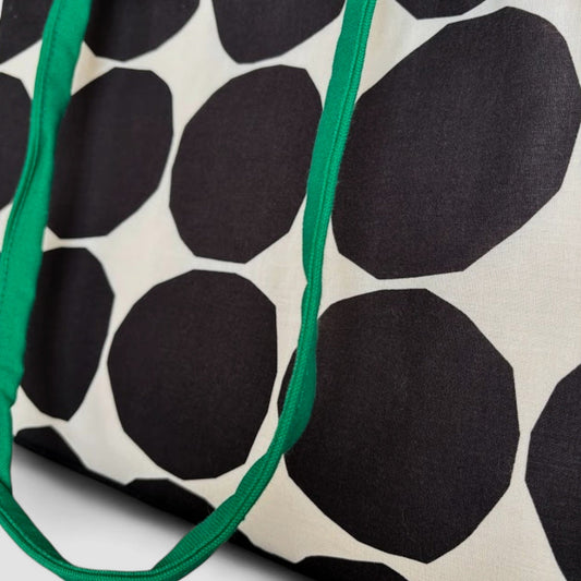 Close-up of a white tote bag with big black polka dots and green shoulder straps.