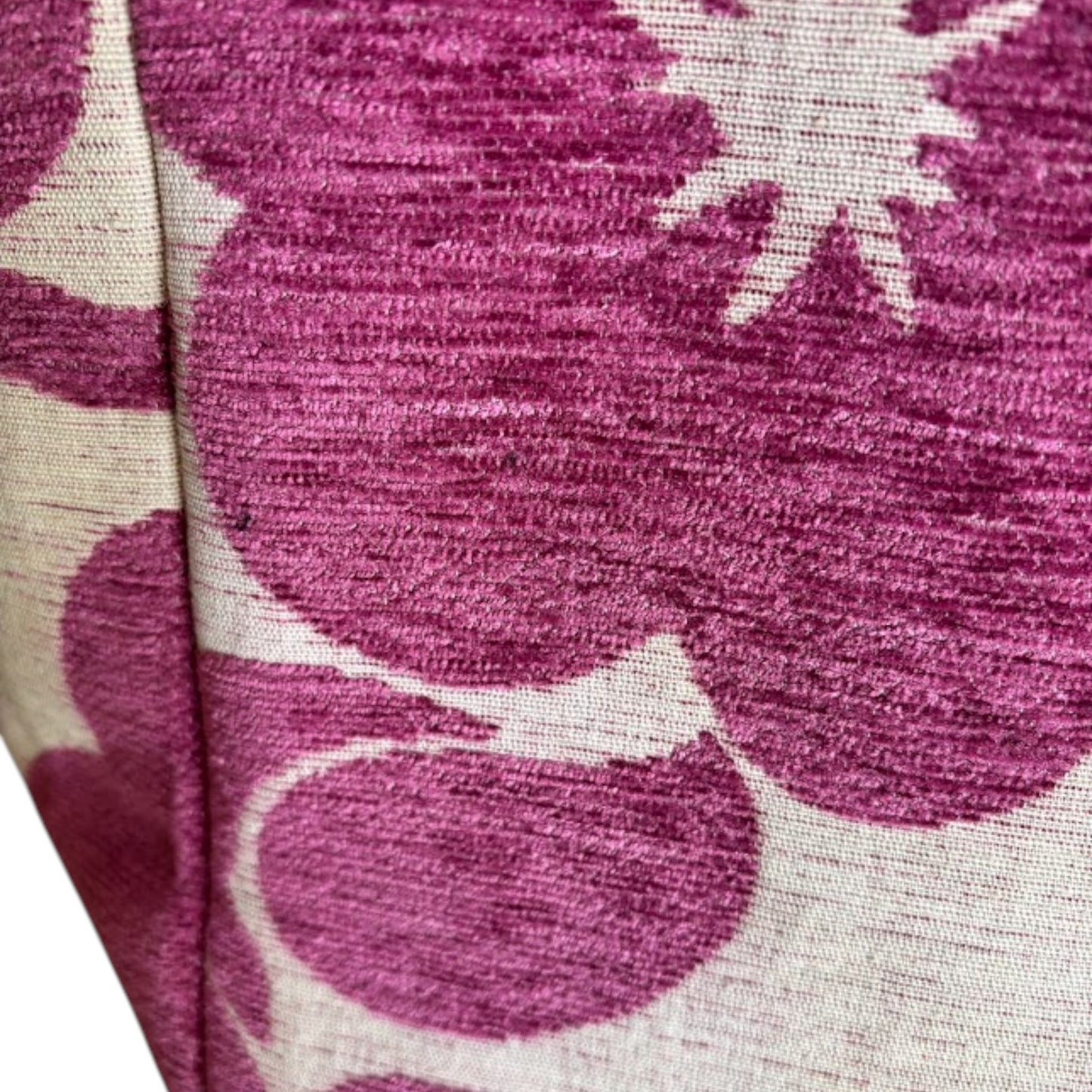 Close up of a textured beige fabric with bold magenta floral patterns.