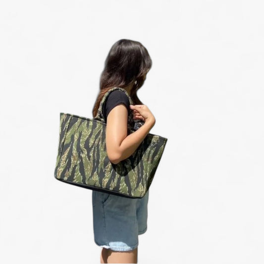 A woman is carrying a stylish green and black camouflage tote bag over their shoulder.