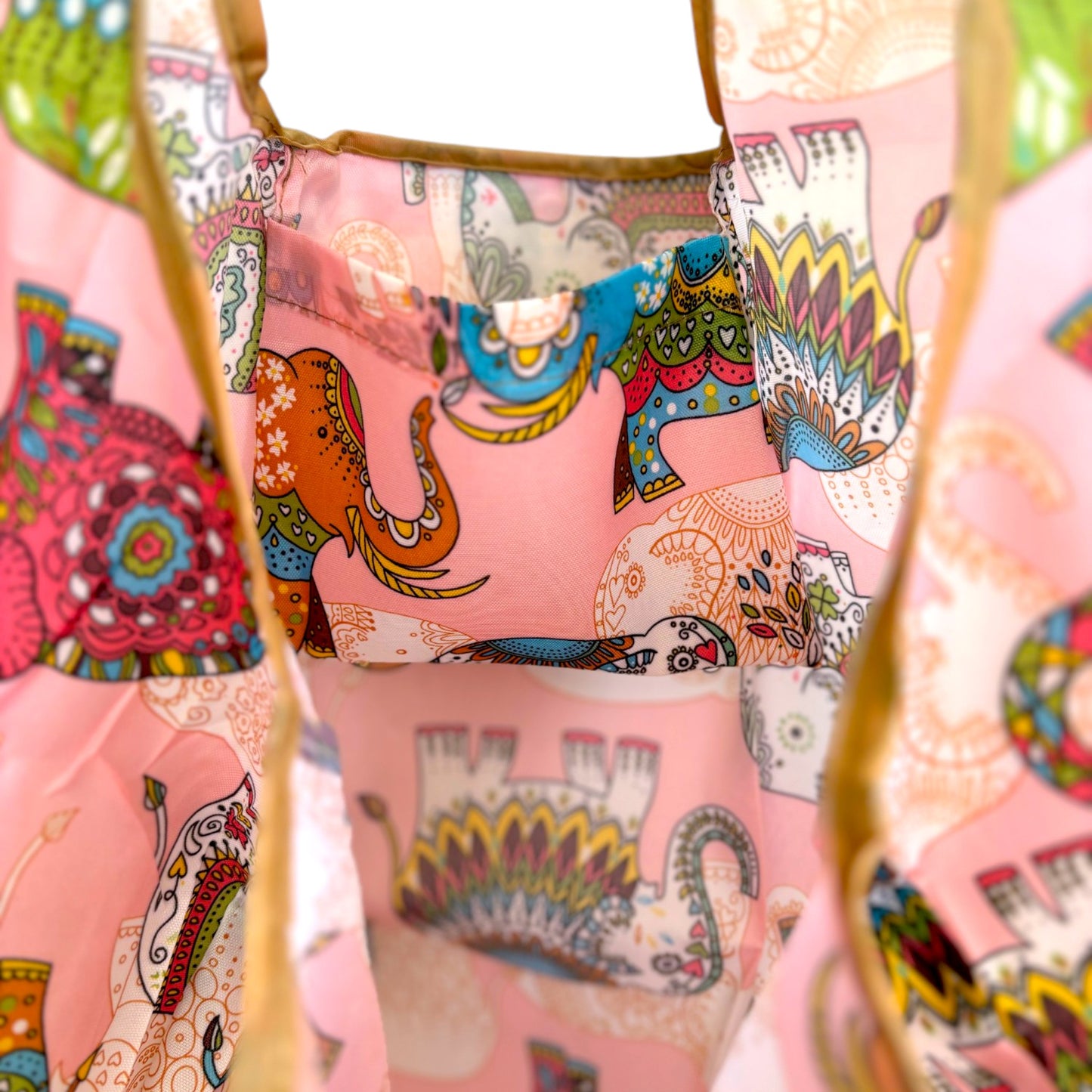 Interior of a pink nylon tote bag with colourful elephant patterns showing a pocket and its large capacity.