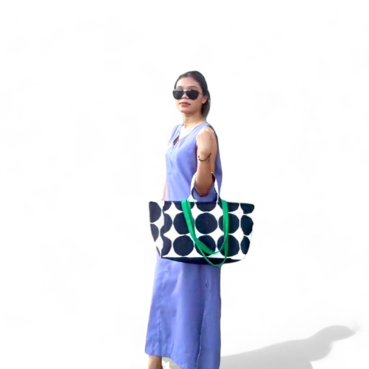 A woman is carrying a large black and white polka dot tote bag in the crook of her arm.