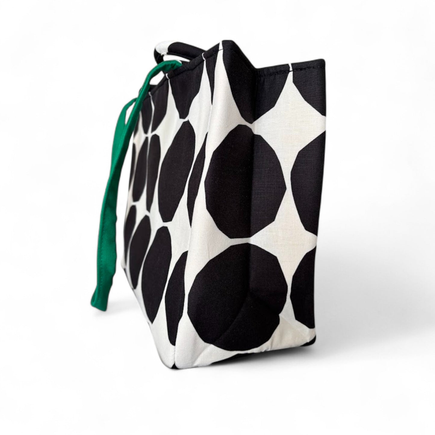 Side view of a back and white polka dots tote showing a green shoulder strap.