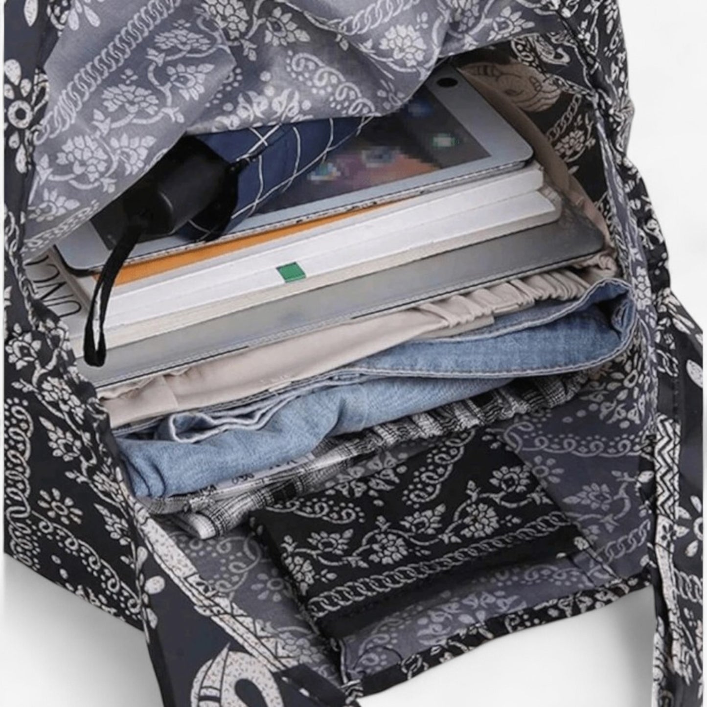 An open, dark brown and white elephant pattern tote bag containing a laptop, books, an umbrella, and clothes.