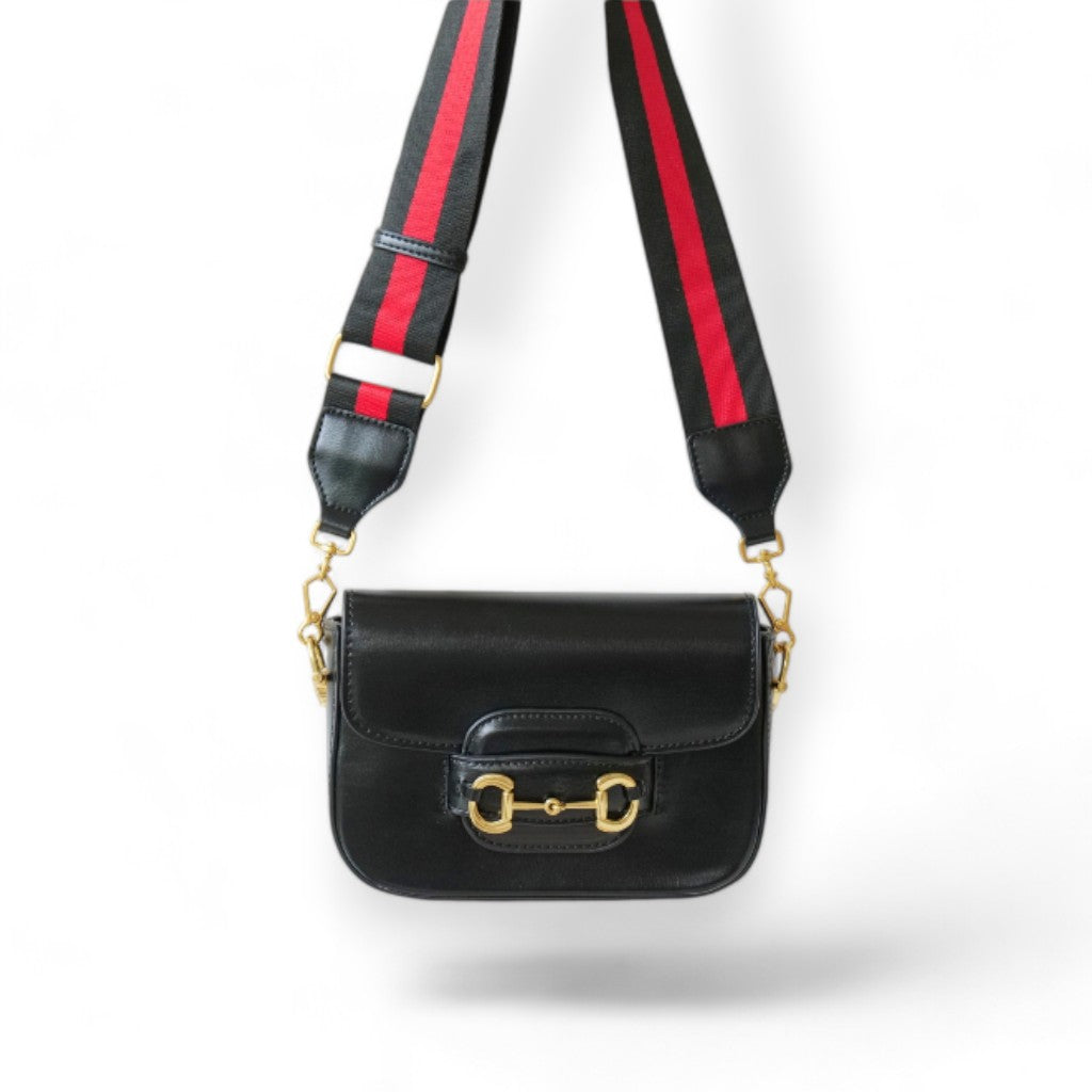 A black leather handbag with a wide red and black nylon strap hanging on the wall.