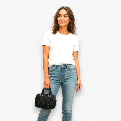 A woman carrying the top handles of a black handbag with a quilted pattern.  