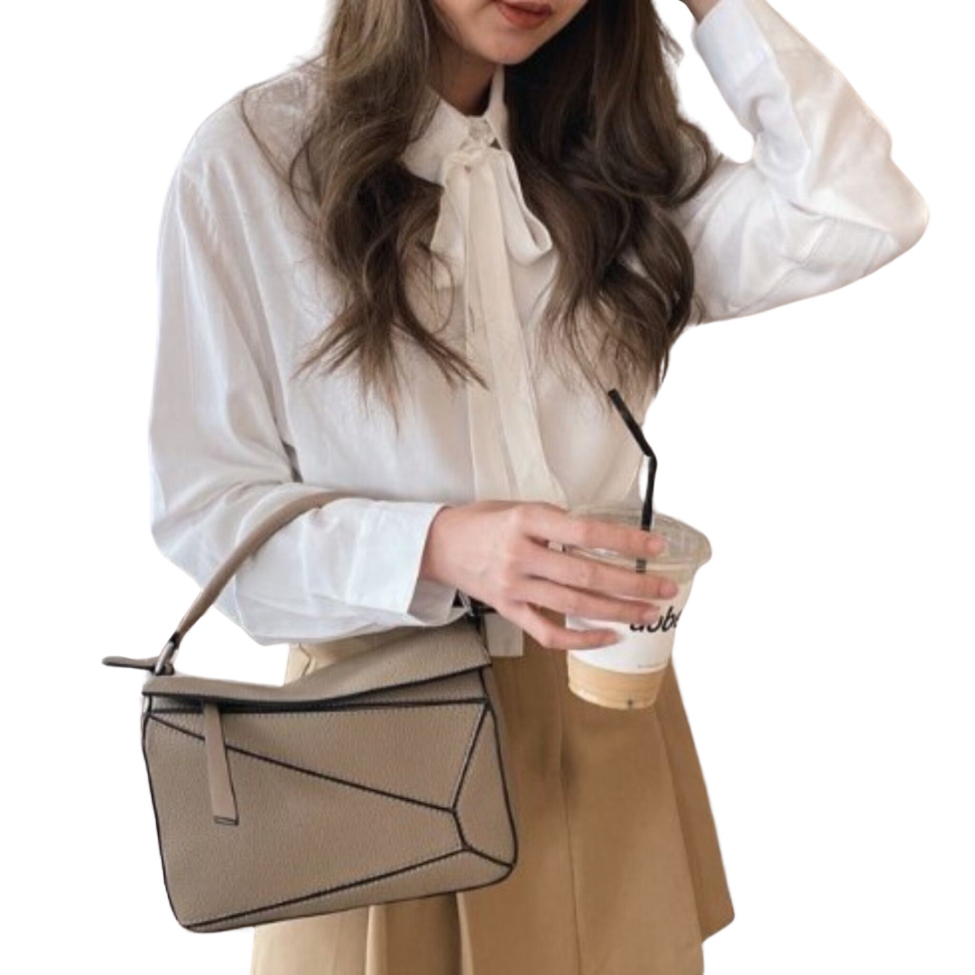 Woman carrying Amy vegan leather handbag in Sand by top handle, resting in the crook of her arm; features geometric panels.