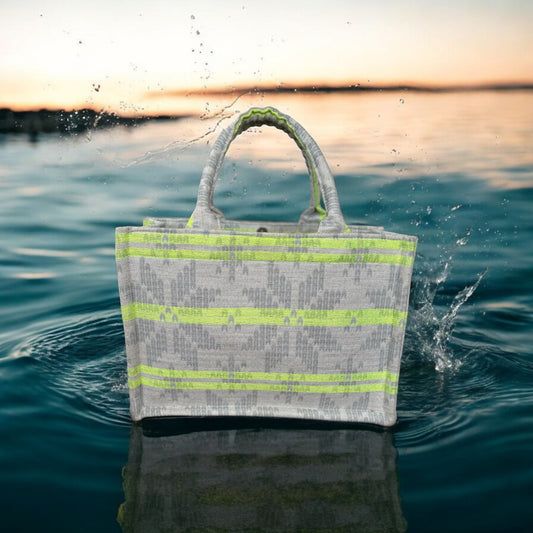 A tote bag with neon green stripes on light grey jacquard fabric, sitting on top of a pool of dark blue water. 