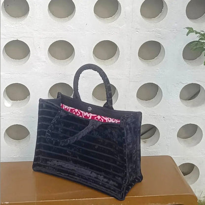 A top view of a spacious, velvety black tote bag with bright raspberry damask-patterned lining and top handles.