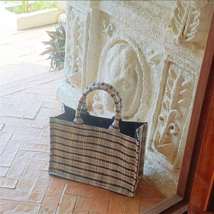 A sturdy tote with strong handles made with white tweed fabric with black, red, and blue threads is sitting outdoor.