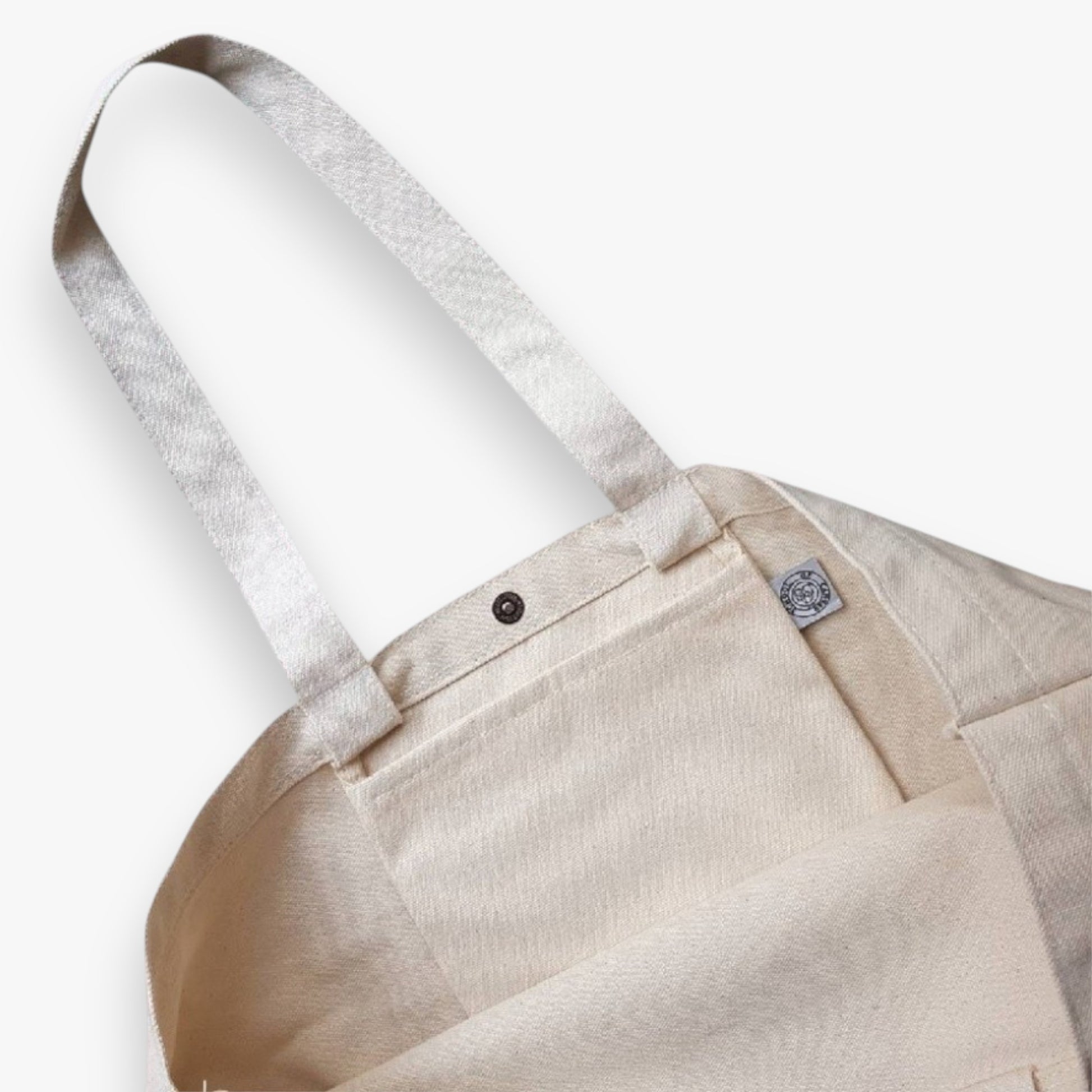 Café Hopper tote close-up view showing a shoulder strap, pocket and magnetic button closure.
