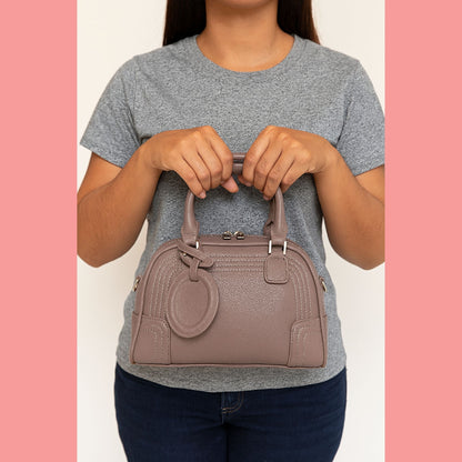 A model holding a modern and chic taupe Boston bowler bag by its top handles in front of her.