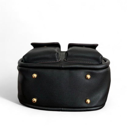 Bottom view of black faux leather Dougie bag with two front flap pockets and 4 gold-tone stud feet hardware.