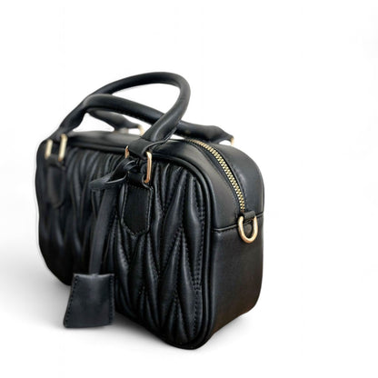 Angle view of black handbag with a quilted pattern, featuring gold-tone hardware and top handles. 