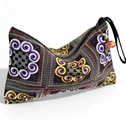 Handmade Hmong embroidered wristlet clutch with bold purple and yellow motifs on a side angle.