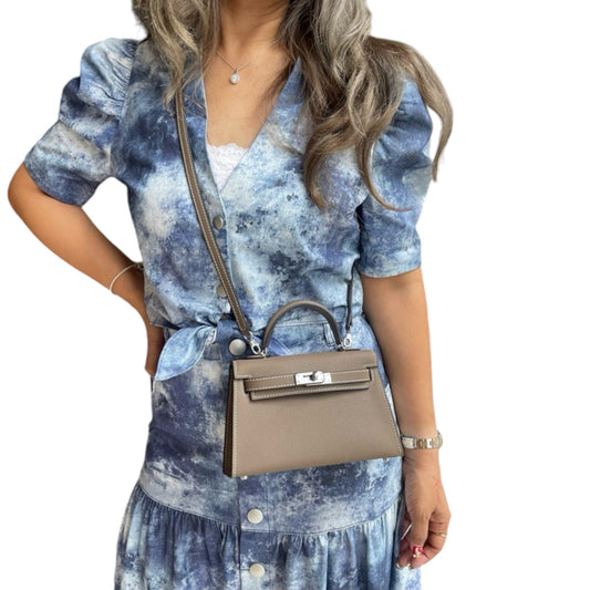 A woman with a taupe structured mini bag with a top handle, worn across her body. 