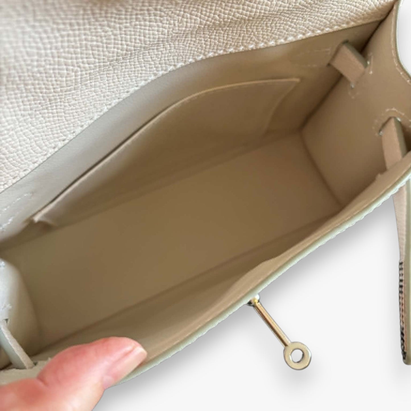 Spacious interior of a white handbag with a turn-lock and a slip pocket.